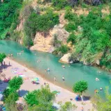 Gente disfrutando del sol y el agua cristalina en el balneario de Montanejos, rodeado de exuberante vegetación y rocas.