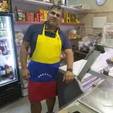 Hombre con delantal de Venezuela en el mercado de Torrefiel, rodeado de productos en neveras y estanterías.