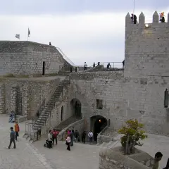El castillo del Papa Luna en Peñíscola, con sus murallas de piedra y escalinatas, recibe a visitantes que pasean por sus patios.