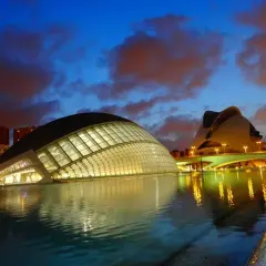 La **Ciudad de las Artes y las Ciencias** de Valencia, con sus icónicos edificios futuristas, se refleja en el agua al anochecer, bajo un cielo dramático.