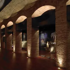 Pasillo del museo de historia de Valencia, con arcos de ladrillo, iluminación tenue y vitrinas con artefactos antiguos.