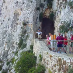 Grupo de excursionistas en el sendero del Peñón de Calpe, con una cueva a la izquierda y vistas rocosas.