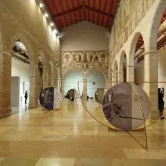 Exposición en el Almudín de Valencia, con arcos de piedra, murales antiguos y paneles circulares que narran la historia del Santo Cáliz.