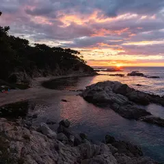 Atardecer en la punta estrella Moraira, con el sol asomando entre rocas y el mar reflejando los tonos rosados del cielo.