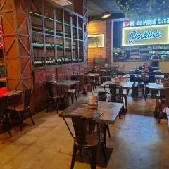 Interior de Jenkins Valencia, un restaurante con mesas de madera, sillas metálicas y un letrero de neón que dice "Love at First Bite Jenkins".