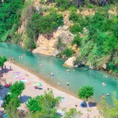 Gente disfrutando del sol y el agua cristalina en el balneario de Montanejos, rodeado de exuberante vegetación y rocas.