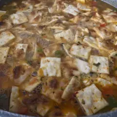 Gazpacho marinero alicantino burbujeante en una sartén, con trozos de pan tostado y verduras.