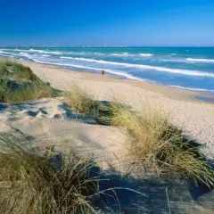 Dunas de arena y hierba en la playa los viveros, con el mar azul y olas rompiendo.