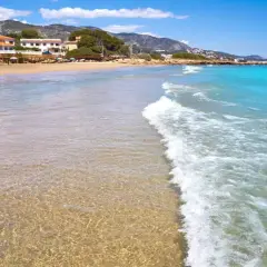 Aguas cristalinas y arena dorada en la playa la Romana, Alcossebre. Un paraíso mediterráneo con montañas al fondo.