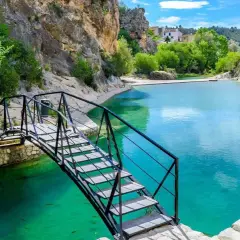 Puente metálico sobre las aguas turquesas del **río Bolbaite**, rodeado de rocas y vegetación exuberante.
