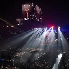 Un artista en un escenario iluminado por focos, con pantallas gigantes mostrando su imagen. ¡Imagina los conciertos Valencia 2026!