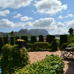 El jardín de l'albarda, con piscina azul, setos verdes, mesa y sillas, y montañas al fondo bajo un cielo nublado.