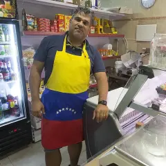 Hombre con delantal de Venezuela en el mercado de Torrefiel, rodeado de productos en neveras y estanterías.