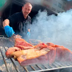 Hombre con guantes azules cocina carne en una parrilla humeante, un festín de carne en el **meat carnival Valencia**.