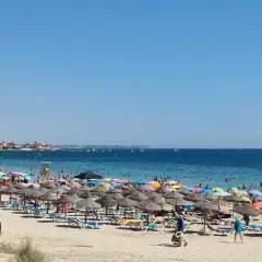 Día soleado en la playa de las Higuericas, con mucha gente disfrutando del mar y la arena bajo coloridas sombrillas.
