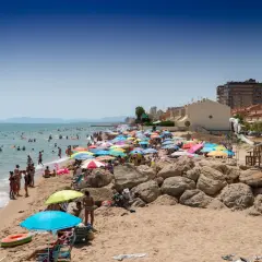 Día soleado en la playa Tavernes de la Valldigna, con mucha gente disfrutando del mar y la arena bajo coloridas sombrillas.