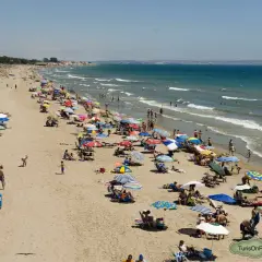 Gente disfrutando del sol y el mar en la playa la marina, con sombrillas de colores y aguas tranquilas.