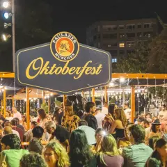 Gente disfrutando en un evento de Oktoberfest Valencia, con luces y un gran cartel de Paulaner.