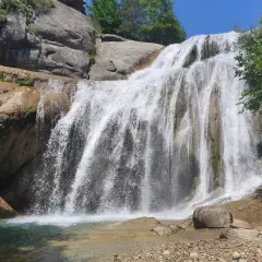 Cascada del Moli, con agua cayendo sobre rocas y vegetación exuberante, formando una piscina natural.