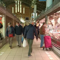 Gente comprando en el mercat central d'Alacant, con puestos de embutidos y carnes.
