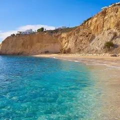 Aguas cristalinas y playas tranquilas en Alicante, con acantilados dorados y casas blancas en la cima.
