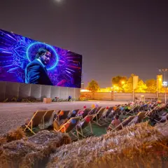 Noche de cine al aire libre en Valencia. Gente relajada en tumbonas viendo una película en pantalla gigante.
