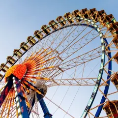 La noria iluminada, una de las atracciones principales de la feria de Valencia, se alza contra el cielo azul.