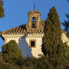 Campanario de piedra con campana, parte del castillo de Villamalefa, rodeado de vegetación y bajo un cielo azul.