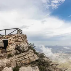 Pequeña construcción de piedra en la cima de una montaña, con barandilla de madera y vistas al valle. El garbí sopla suavemente.