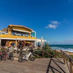 Restaurante Nautilus en la playa Punta Prima, con gente disfrutando en terrazas y bicicletas aparcadas.
