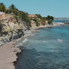 Acantilados y calas rocosas con aguas turquesas, perfectas para descubrir las playas cerca de Calpe. Windsurfistas disfrutan del mar.