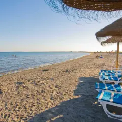 Tumbonas y sombrillas en la playa la gola santa pola, con el mar azul y gente disfrutando del sol.