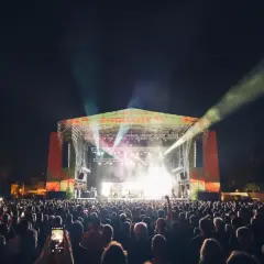 Multitud disfrutando de los **concerts de Vivers** bajo un cielo nocturno iluminado por focos y la energía de la banda en el escenario.