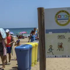 Cartel en la playa de El Carabassí, Alicante, indica "Playas sin humo". Familias disfrutan del sol y el mar.