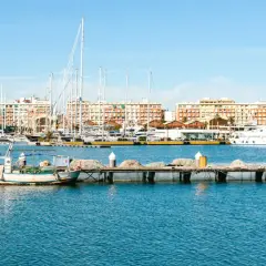 Barcos de pesca y yates de lujo atracados en la marina de Valencia, con edificios coloridos de fondo bajo un cielo azul.