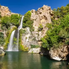 El Salto de Chella, una cascada imponente rodeada de rocas y vegetación exuberante, cae en una poza de agua verde.