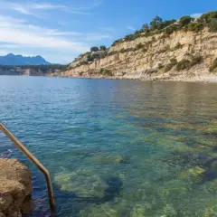 Escalera metálica para acceder a las aguas cristalinas de cala Punta Estrella, con acantilados y montañas al fondo.