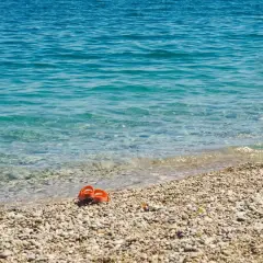 Chanclas naranjas abandonadas en la **playa Malvarrosa de Corinto**, esperando a su dueño junto a las aguas cristalinas.