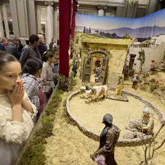 Niños observan un detallado belén en el Ayuntamiento de Valencia, con figuras que recrean la vida en un pueblo antiguo.