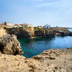 Explora la isla de Tabarca: casas blancas sobre acantilados rocosos, aguas cristalinas y barcos en el horizonte. Un lugar para descubrir.