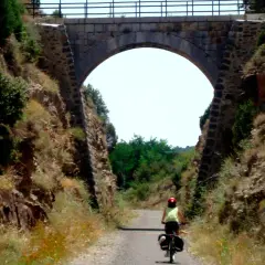 Ciclista pedalea por la vía verde Valencia bajo un antiguo puente de piedra.