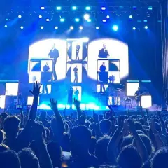 Multitud en concierto de Vetusta Morla en Valencia. Luces azules y pantallas con imágenes de los miembros de la banda crean un ambiente electrizante.
