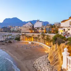 Atardecer en la playa Poniente de Benidorm, con el mar azul, la arena dorada, palmeras y edificios modernos.