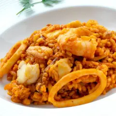 Arroz del senyoret con gambas, calamares y trozos de pescado blanco, servido en un plato blanco.