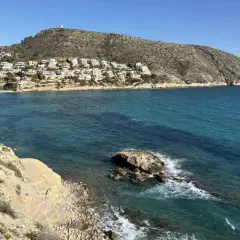 Vista de calas y acantilados con casas blancas en la ladera, aguas turquesas y un peñasco en el mar. Playas bonitas cerca de Benidorm.