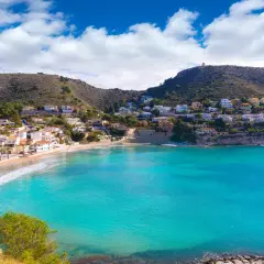 Bahía de aguas turquesas en cala el Portet, con casas blancas y verdes colinas.