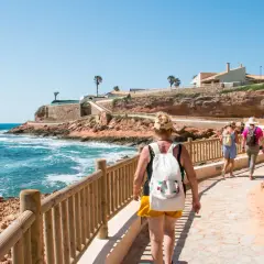 Paseo por la costa en cala capitan. Turistas caminan por un sendero con vistas al mar azul y acantilados rojizos.