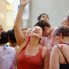 Gente feliz y empapada de tomate en la Tomatina, con una mujer riendo a carcajadas y el brazo en alto.