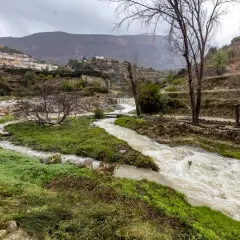 Río caudaloso cerca de Sella, Alicante, con cascadas y un pueblo blanco en la ladera.