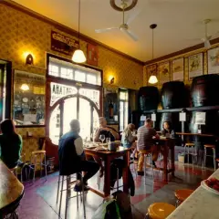 Gente en un bar tradicional, con barriles y carteles antiguos. Un lugar con encanto, como una casa de montaña en Valencia, donde disfrutar de tapas y vermut.